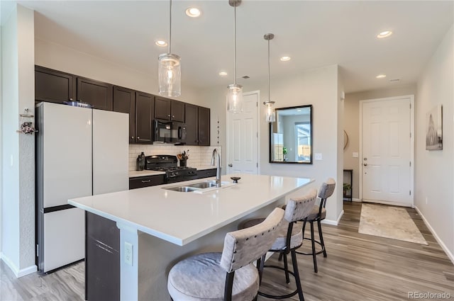 kitchen featuring sink, a kitchen breakfast bar, pendant lighting, an island with sink, and black appliances