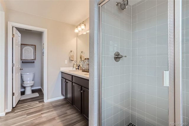 bathroom featuring tiled shower, hardwood / wood-style flooring, vanity, and toilet