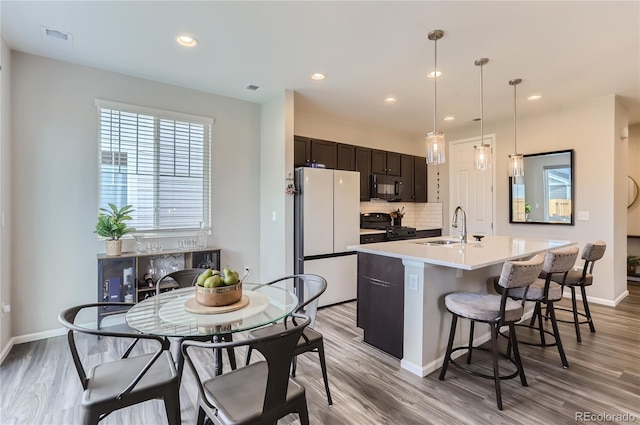 kitchen with sink, decorative light fixtures, light hardwood / wood-style flooring, a center island with sink, and black appliances