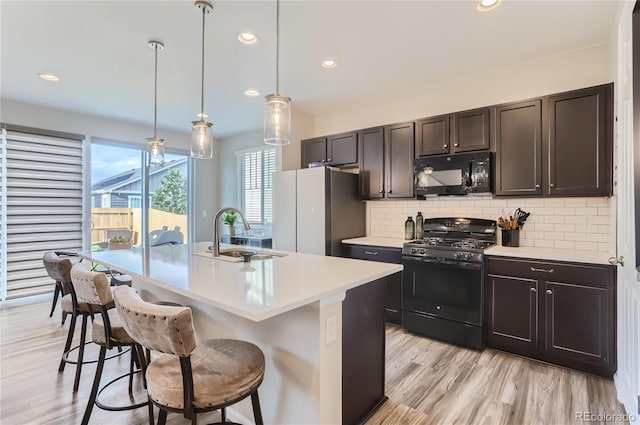 kitchen with pendant lighting, a center island with sink, black appliances, a kitchen bar, and sink