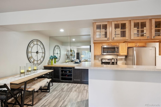 kitchen featuring tasteful backsplash, sink, light hardwood / wood-style floors, kitchen peninsula, and stainless steel appliances