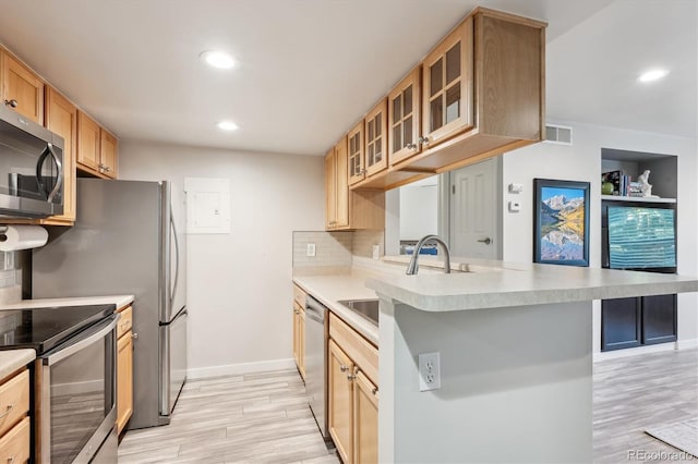 kitchen with a kitchen bar, light wood-type flooring, kitchen peninsula, stainless steel appliances, and decorative backsplash