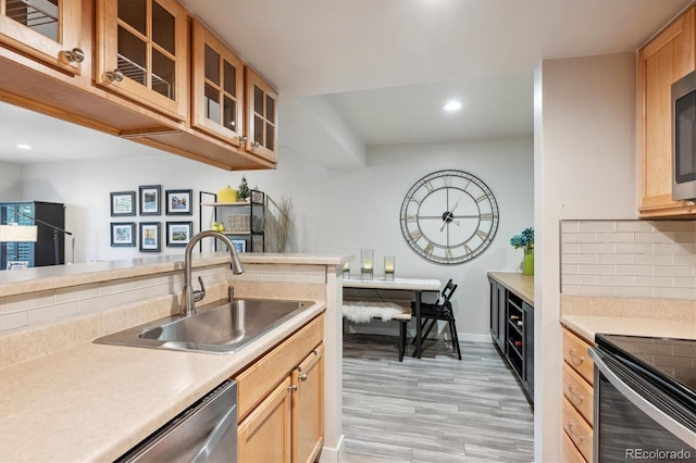 kitchen with tasteful backsplash, appliances with stainless steel finishes, sink, and light hardwood / wood-style floors