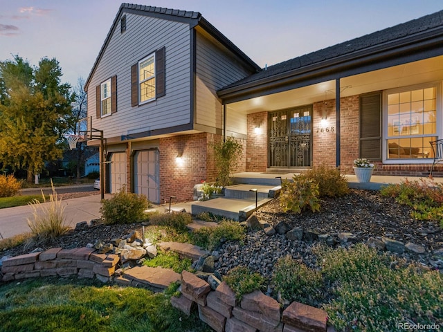 exterior space featuring a porch, brick siding, driveway, and an attached garage