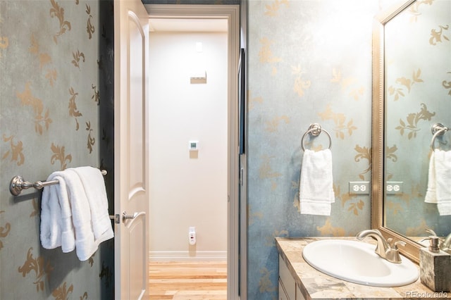 3143 Elmira St, Denver, CO 80238 - bathroom featuring vanity, wood finished floors, wallpapered walls, and baseboards