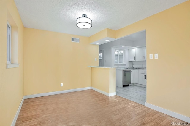 kitchen with white cabinetry, dishwasher, sink, a textured ceiling, and light wood-type flooring