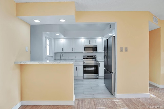 kitchen featuring white cabinets, appliances with stainless steel finishes, light wood-type flooring, and kitchen peninsula