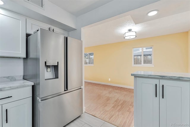 kitchen with light stone countertops, stainless steel refrigerator with ice dispenser, light wood-type flooring, and white cabinetry