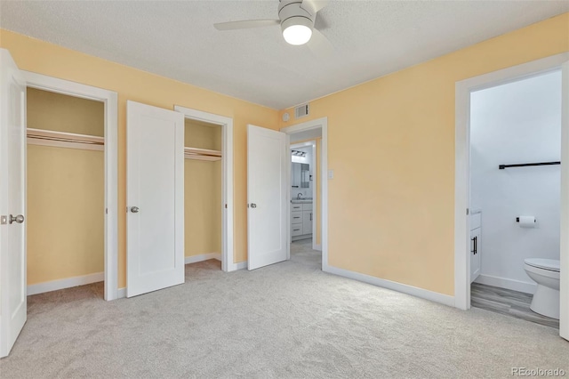 unfurnished bedroom featuring light carpet, connected bathroom, ceiling fan, and multiple closets