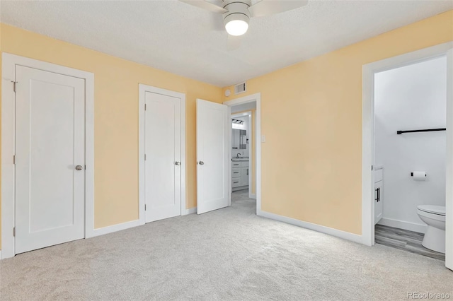 unfurnished bedroom featuring ceiling fan, light colored carpet, and ensuite bath