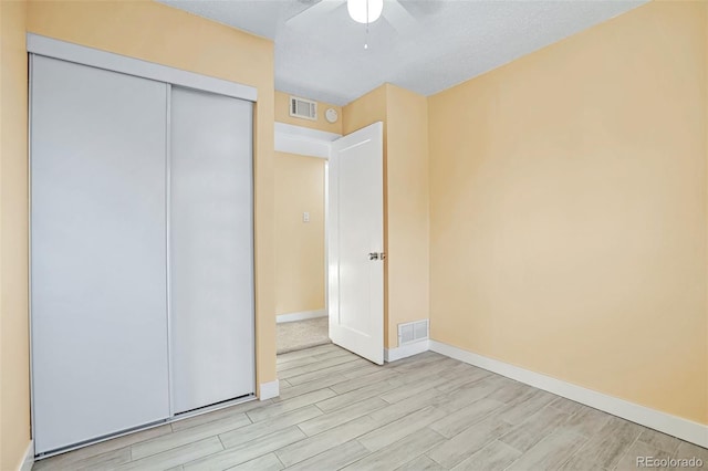 unfurnished bedroom featuring a textured ceiling, a closet, light hardwood / wood-style flooring, and ceiling fan