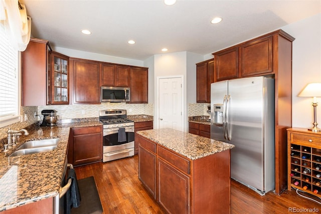 kitchen with stone countertops, a sink, appliances with stainless steel finishes, a center island, and dark wood finished floors