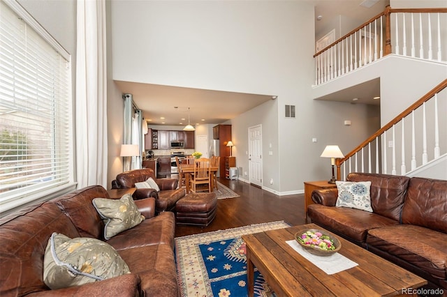 living room with dark wood-type flooring, a high ceiling, visible vents, baseboards, and stairway