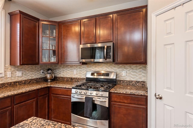 kitchen with appliances with stainless steel finishes, dark stone countertops, backsplash, and glass insert cabinets