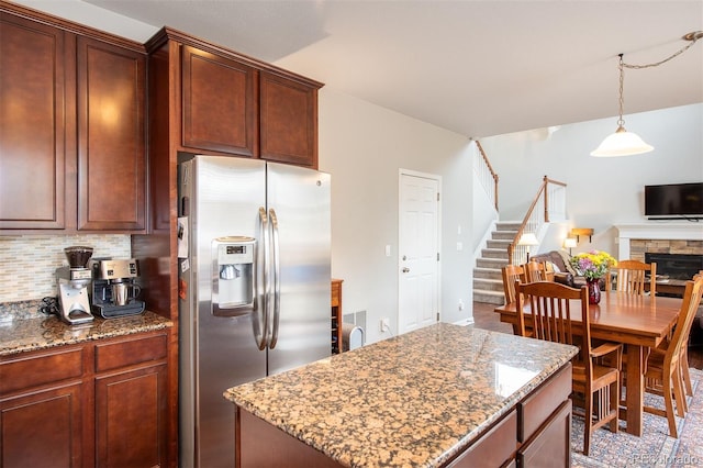 kitchen featuring a stone fireplace, tasteful backsplash, stainless steel fridge, and light stone countertops