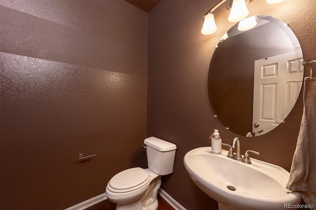 half bath featuring a textured wall, a sink, toilet, and baseboards