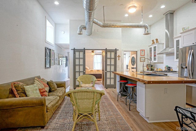 kitchen with wall chimney range hood, light wood-type flooring, a kitchen breakfast bar, wood counters, and a high ceiling