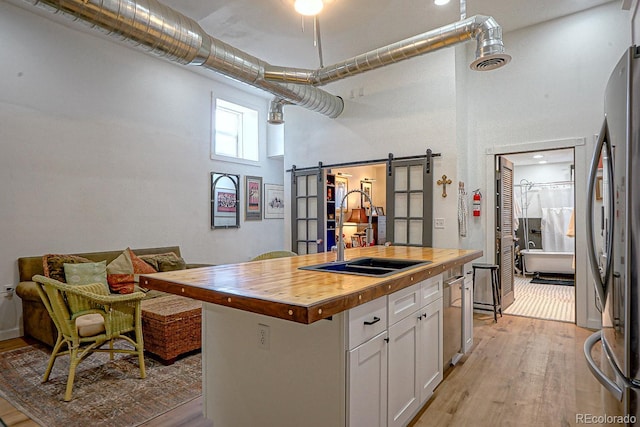 kitchen with light wood-type flooring, wood counters, stainless steel refrigerator, a kitchen island, and a barn door