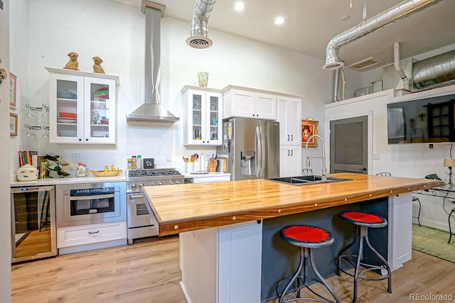 kitchen with appliances with stainless steel finishes, light hardwood / wood-style floors, wall chimney exhaust hood, white cabinets, and wood counters