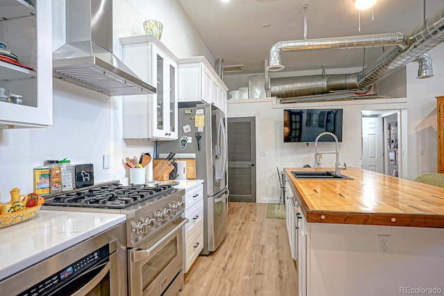 kitchen with high end stainless steel range oven, light wood-type flooring, butcher block countertops, wall chimney range hood, and white cabinets