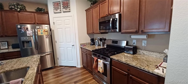 kitchen featuring appliances with stainless steel finishes, light stone countertops, sink, and hardwood / wood-style flooring