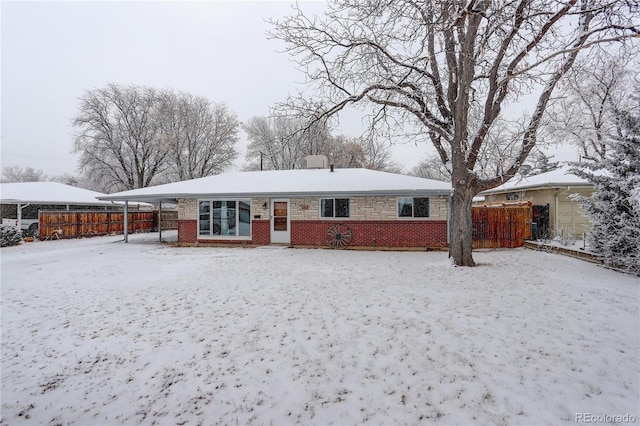 snow covered rear of property with brick siding and fence