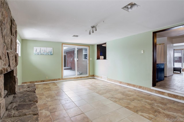 empty room featuring rail lighting, visible vents, a fireplace, and baseboards