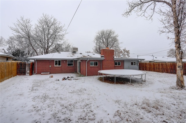 snow covered property with a trampoline, central AC, brick siding, and a fenced backyard