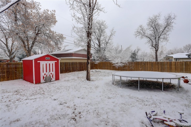 yard covered in snow with a storage shed, a fenced backyard, a trampoline, and an outbuilding