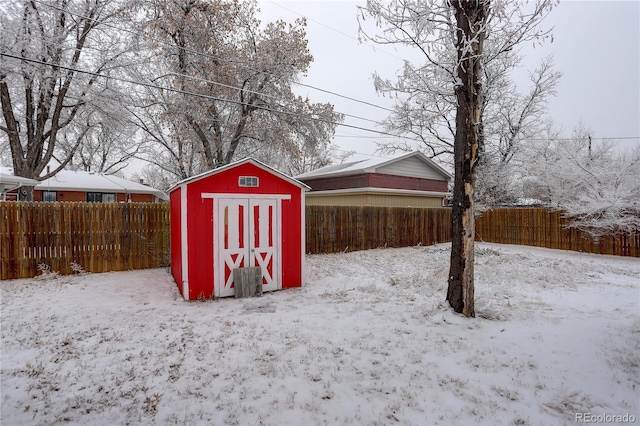 snow covered structure with a shed and a fenced backyard