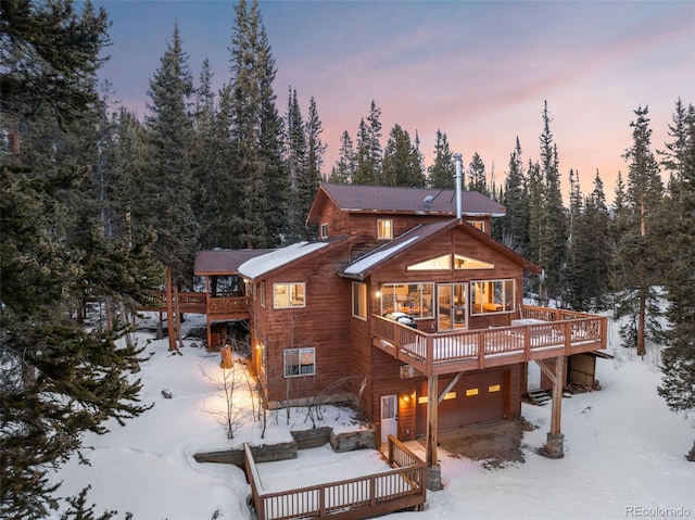 snow covered house featuring a deck and an attached garage