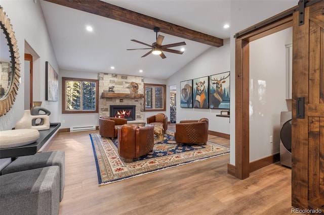 living room with a baseboard radiator, lofted ceiling with beams, a barn door, a stone fireplace, and wood finished floors