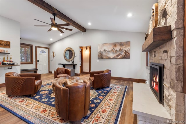 living area with vaulted ceiling with beams, a stone fireplace, baseboards, and wood finished floors