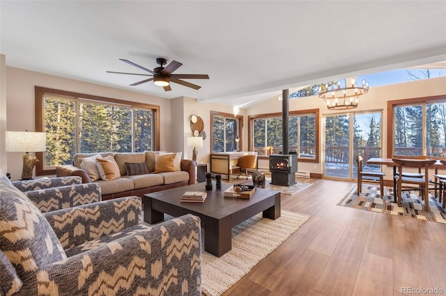 living area featuring ceiling fan with notable chandelier, wood finished floors, a wood stove, and lofted ceiling