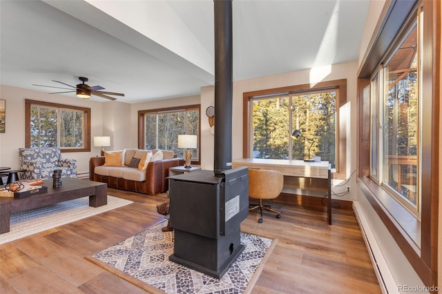 living room with a wood stove, ceiling fan, baseboards, and wood finished floors