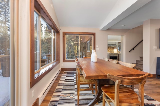 dining room featuring lofted ceiling, a baseboard radiator, wood finished floors, baseboards, and stairs