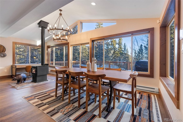 dining space with a wood stove, a wealth of natural light, vaulted ceiling, and wood finished floors