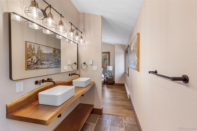 bathroom with wood finished floors, a sink, baseboards, and double vanity