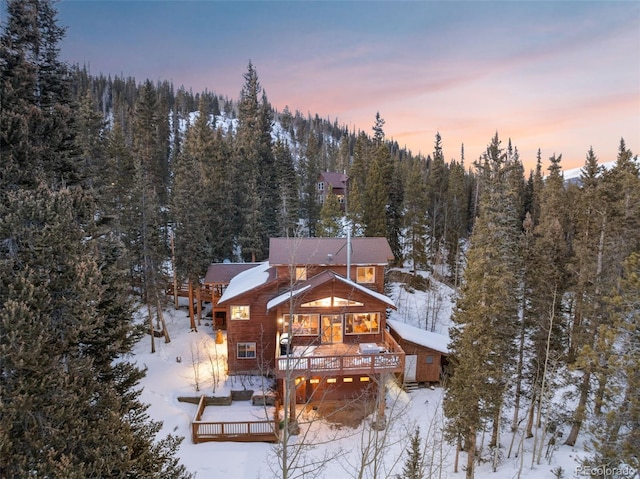 snow covered property featuring a deck and a wooded view