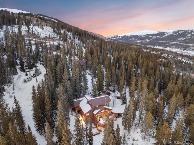 snowy aerial view with a mountain view and a wooded view