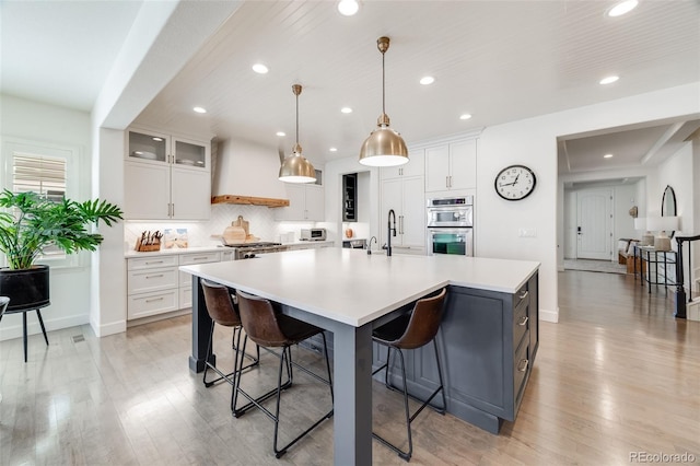 kitchen featuring a breakfast bar, custom exhaust hood, a spacious island, double oven, and light wood-style floors