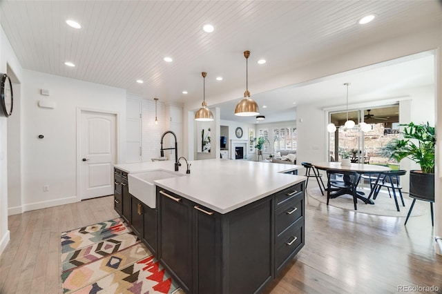 kitchen featuring wooden ceiling, light wood-style flooring, light countertops, dark cabinetry, and a sink