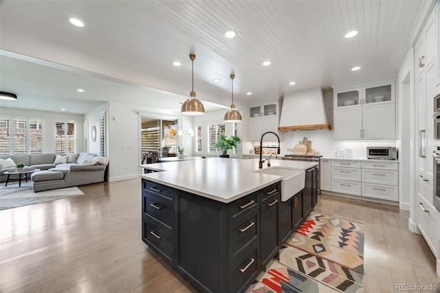 kitchen featuring a sink, premium range hood, white cabinets, and dark cabinetry