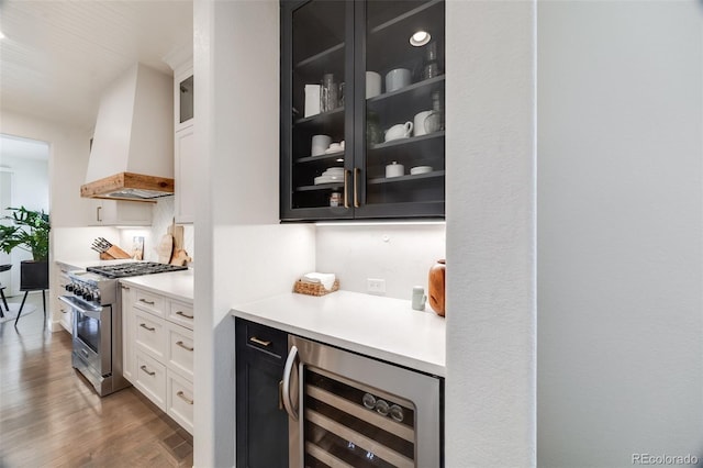 bar featuring beverage cooler, high end stainless steel range oven, wall chimney exhaust hood, and wood finished floors