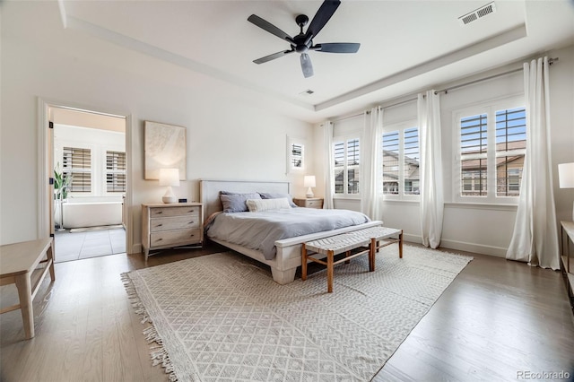 bedroom with baseboards, visible vents, a raised ceiling, and wood finished floors