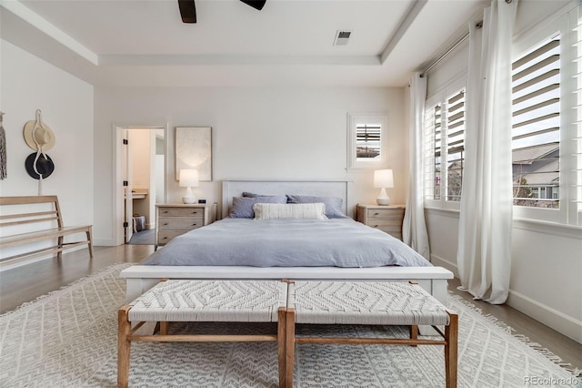 bedroom with light wood finished floors, visible vents, a tray ceiling, and baseboards