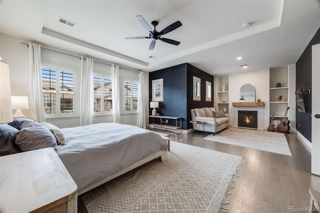 bedroom with a glass covered fireplace, wood finished floors, visible vents, baseboards, and a raised ceiling