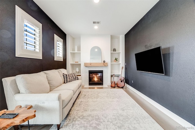 living area with built in shelves, visible vents, a fireplace with flush hearth, wood finished floors, and baseboards