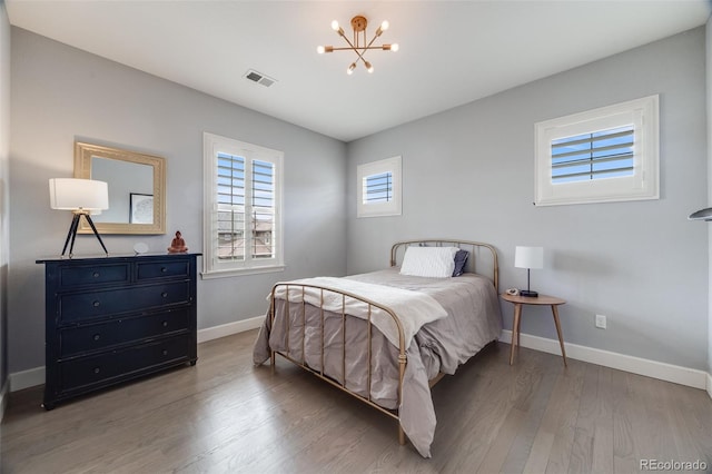 bedroom with baseboards, a notable chandelier, visible vents, and wood finished floors