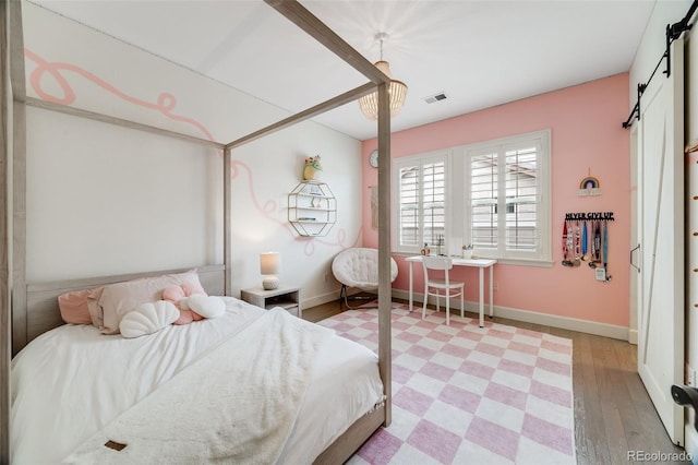 bedroom featuring a barn door, light wood-type flooring, visible vents, and baseboards